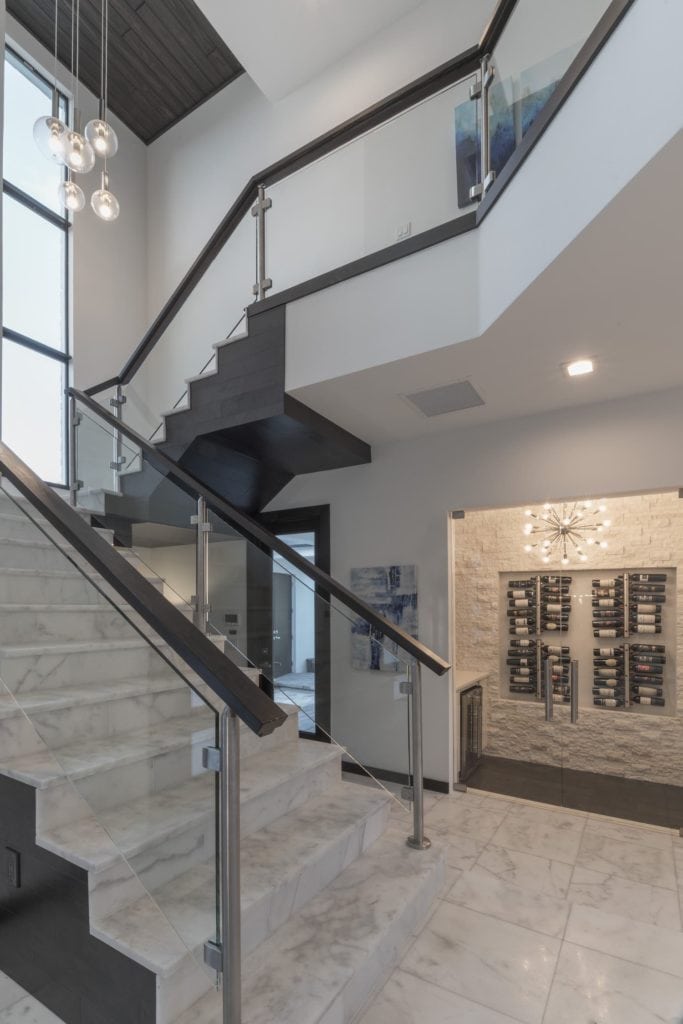 A glass panel staircase framed with chrome supports and wood railings with marble stairs in this Florida Modern Home designed and built by Orlando Custom Home Builder Jorge Ulibarri www.imyourbuilder.com
