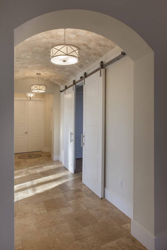 Barn doors painted white with stainless steel hardware open to the media room and the hallway with a barrel travertine tile ceiling. The home was designed and built by Orlando Custom Home Builder Jorge Ulibarri. www.imyourbuilder.com