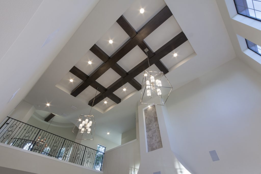 The ceiling treatment in the grand room draws the eye up to the grid of beams and two geometric chandeliers, an open hallway bridges the two wings of the home upstairs overlooking the tower entry and grand room. The home was designed and built by Orlando Custom Home Builder Jorge Ulibarri. www.imyourbuilder.com