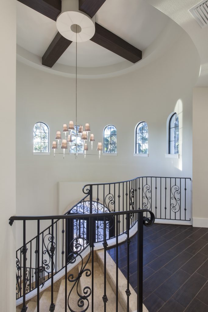 A two-story tower foyer makes a grand entrance pouring in natural light from a crown of windows. The wrought iron staircase echoes the design of the custom made wrought iron and glass door in this home designed and built by Orlando Custom Home Builder Jorge Ulibarri. www.imyourbuilder.com