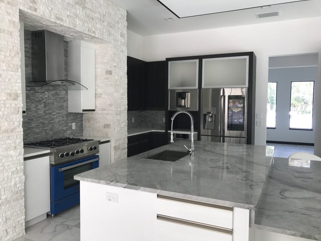 In this Florida-Modern kitchen designed and built by Orlando Custom Homebuilder Jorge Ulibarri, white ledge stone frames the custom-colored blue range, drawing attention to the pop of color. for more go to www.imyourbuilder.com
