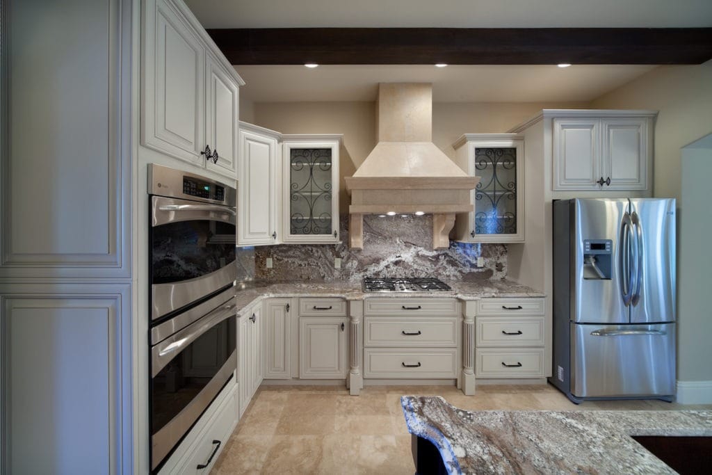 A transitional style kitchen designed and built by Orlando Custom HomeBuilder Jorge Ulibarri that skews traditional with ornate cabinetry, travertine floors and wood beams. The white cabinets and stainless appliances temper the traditional elements. www.imyourbuilder.com 