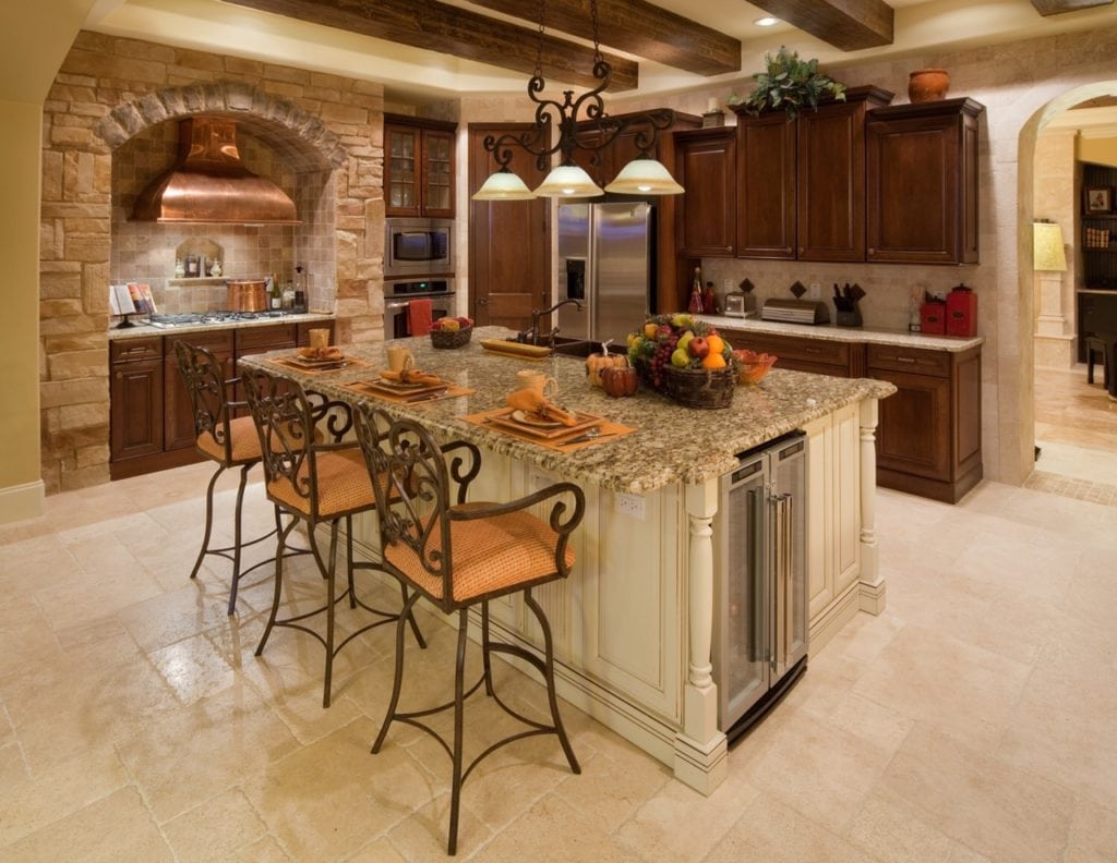 This traditional style kitchen pulls from Tuscan influences such as the copper rangehood framed by stone and kitchen island base cabinetry that mimics furniture with wood carvings and embellishments. www.imyourbuilder.com 