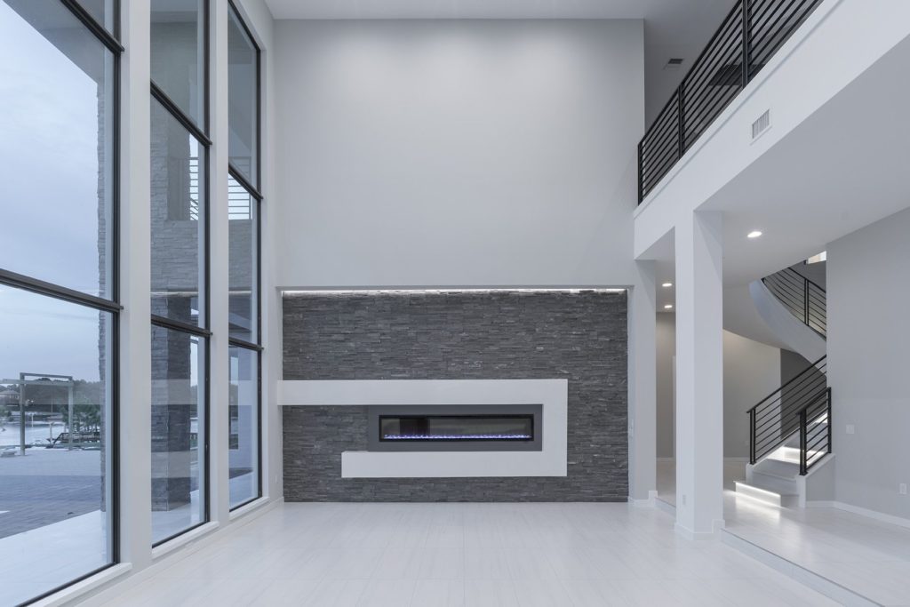In the living room, a 16-foot-long ledgestone stone fireplace runs horizontally from wall-to-wall with a geometric frame of white Venetian plaster around the electric firebox. The fireplace wall is lit with LEDs from above.