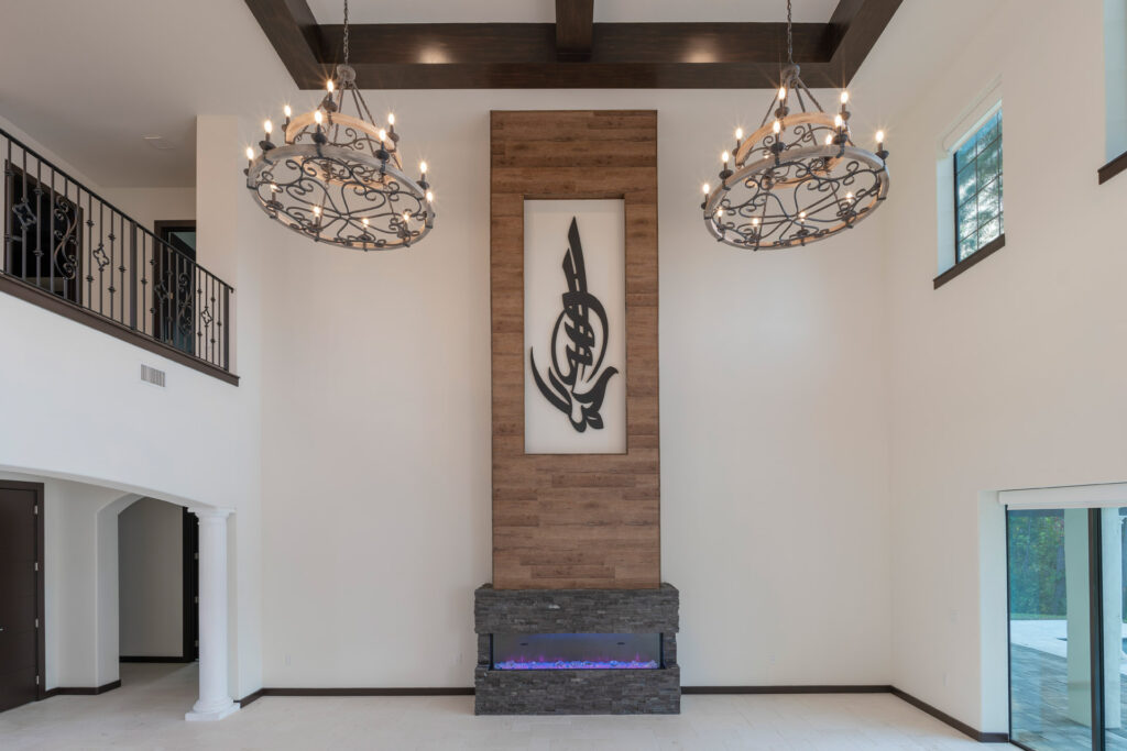 The great room draws focus to an electric fireplace clad in gray stacked stone with a wood plank column that rises above it with an inset to display artwork. The ceilings soar to 22 feet in the great room. The home is designed and built by Orlando Custom Homebuilder Jorge Ulibarri.