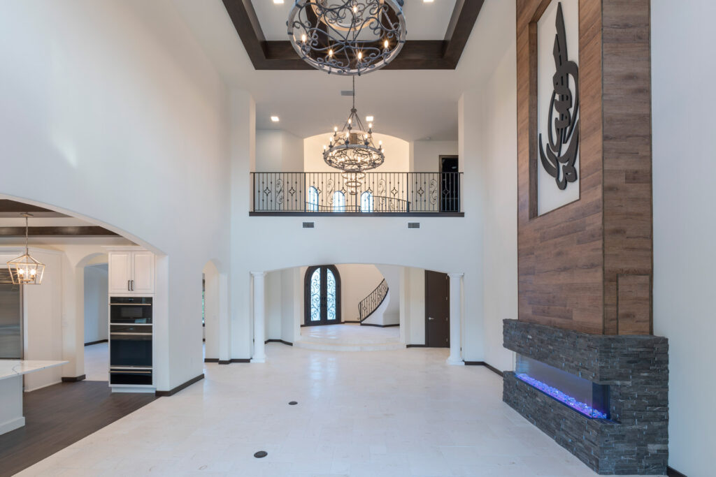 The great room opens to the kitchen with 22 foot high ceilings anchored by two large chandeliers and wood beams. The balcony walkway connects the two wings of the house. The home is designed and built by Orlando Custom Homebuilder Jorge Ulibarri. 