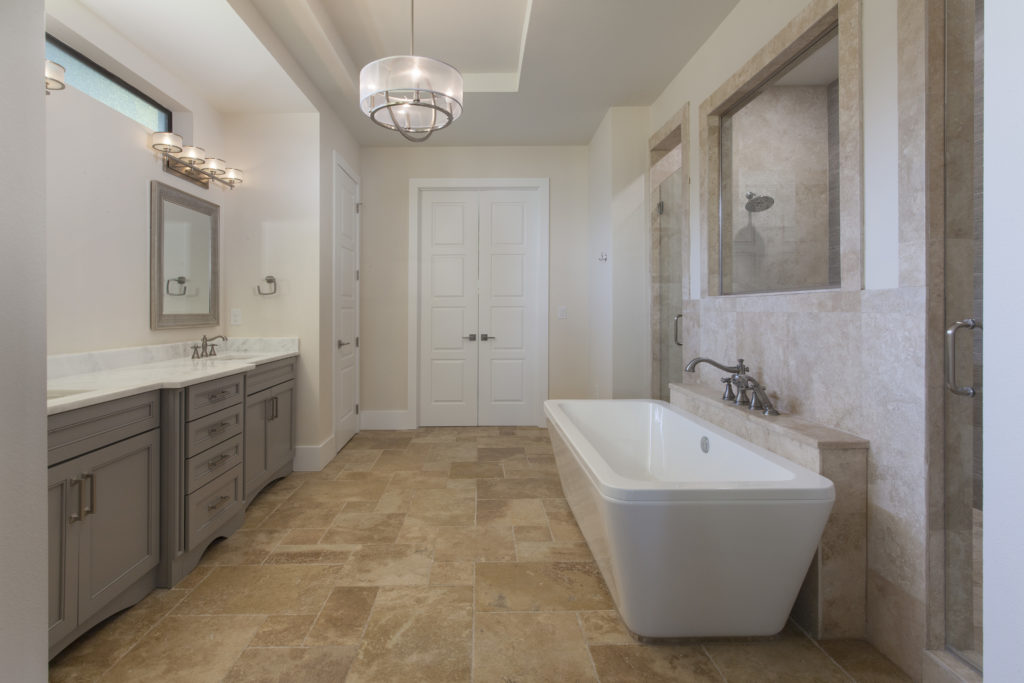 This bathroom by Orlando Custom Home Builder Jorge Ulibarri is illuminated with two vanity light fixtures and a transitional style chandelier. 
